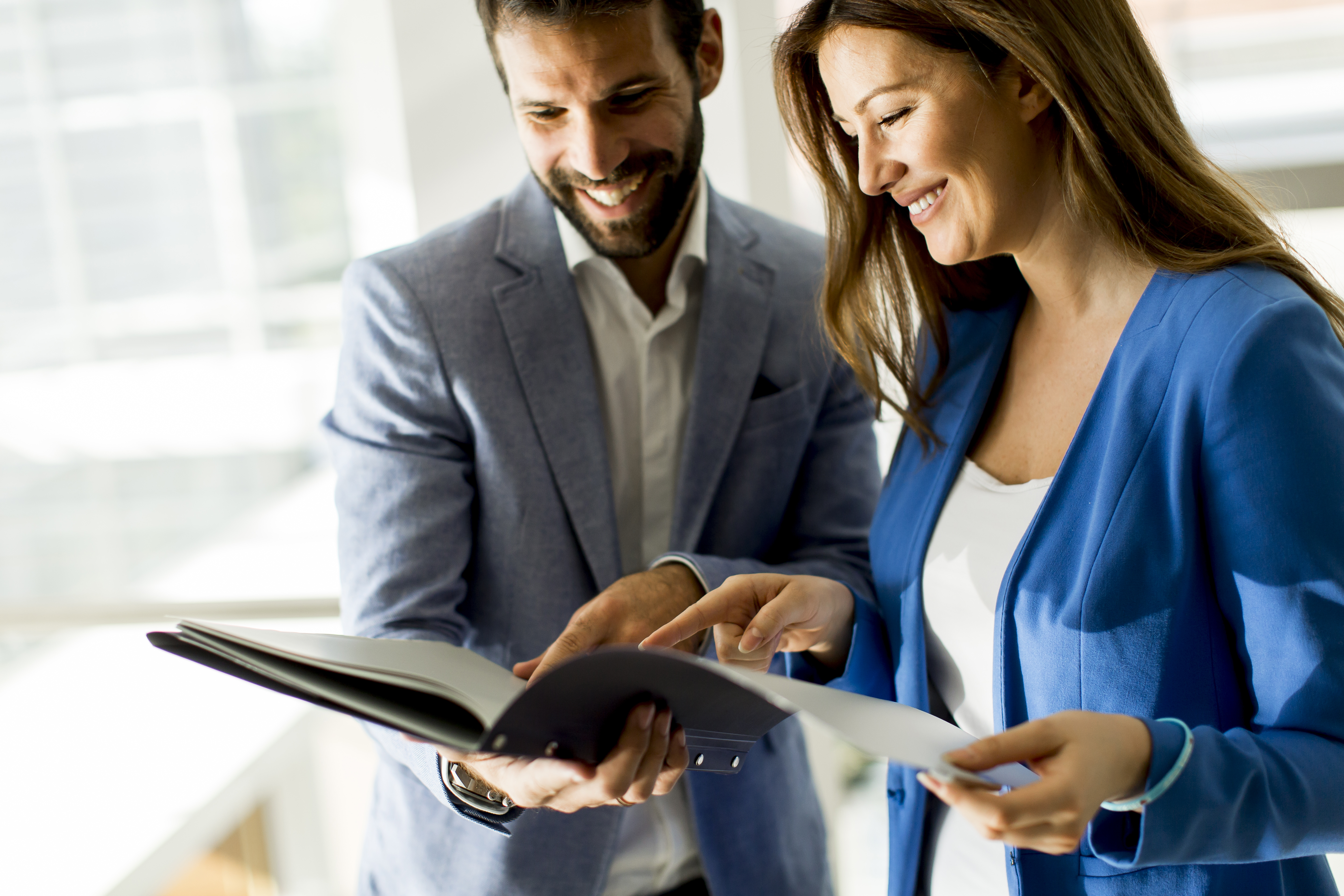 Kobieta i mężczyzna w średnim wieku stoją wsp&oacute;lnie i przeglądają razem dokumenty w biurze