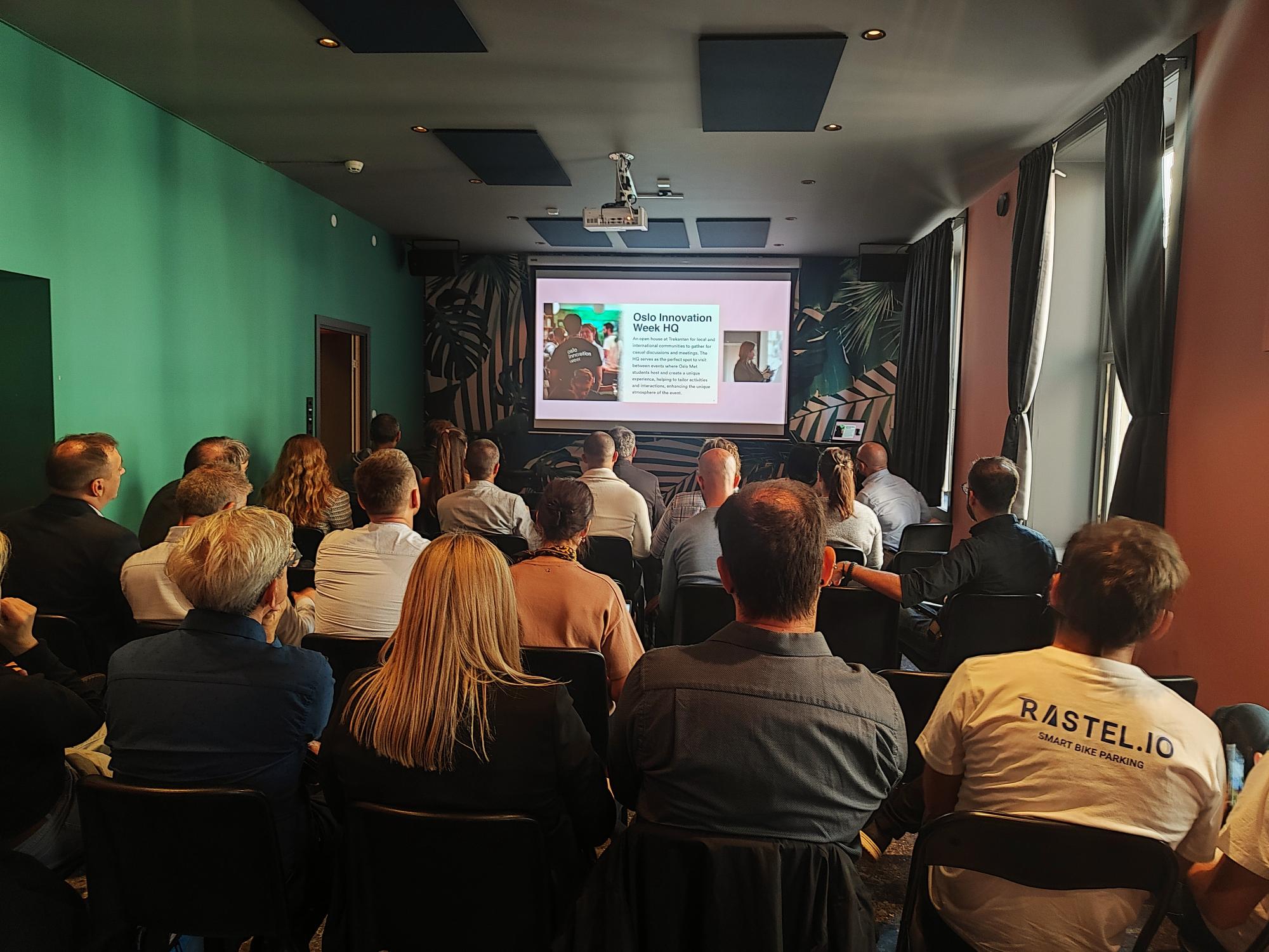 Ludzie siedzą w długiej wąskiej sali i patrzą na ekran projektora