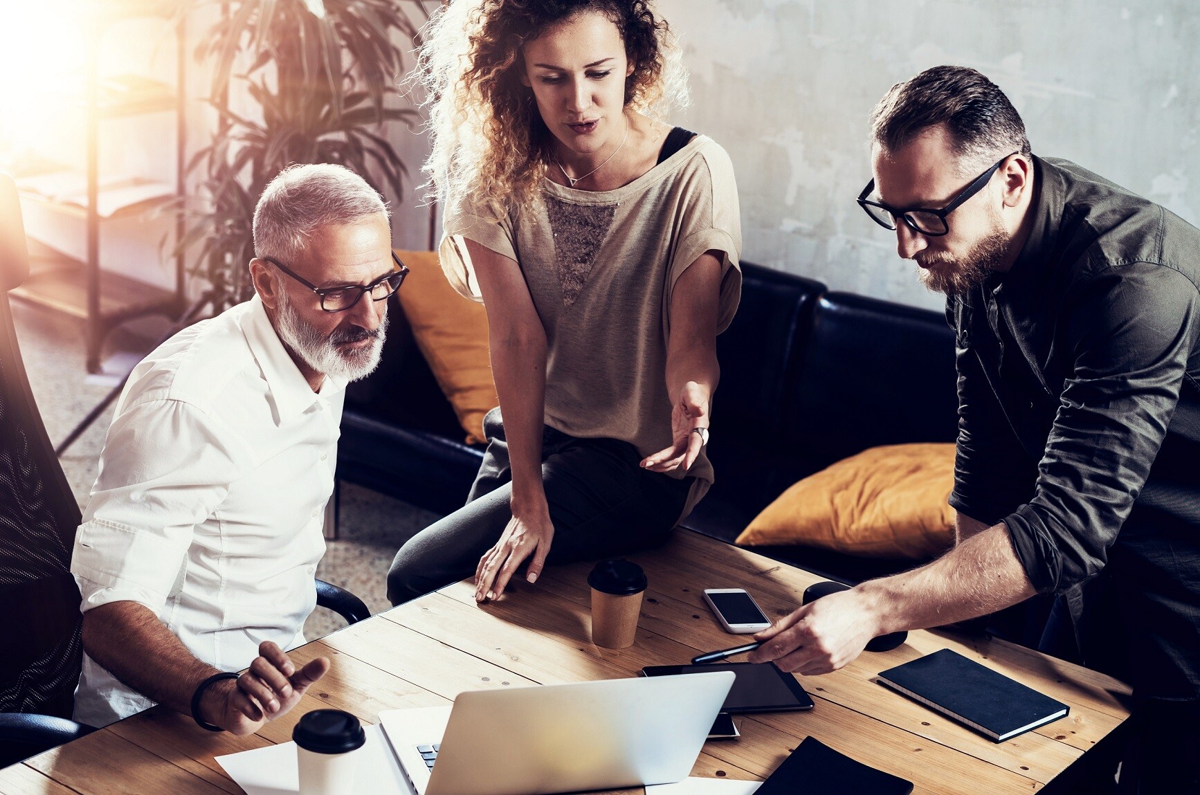 Dw&oacute;ch mężczyzn i kobieta siedzą przy stole i patrzą się w ekran laptopa