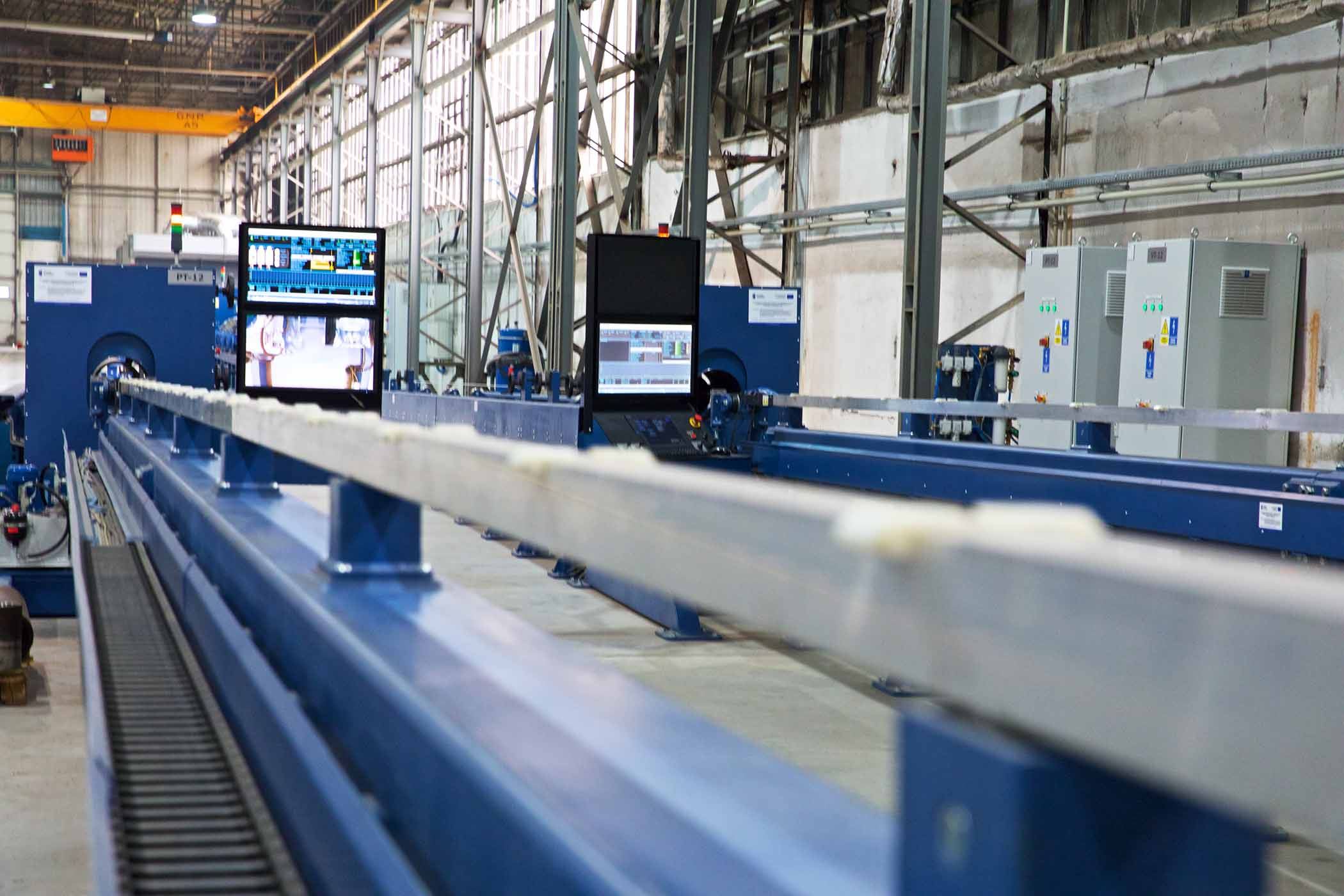Zdjęcie maszyny na hali produkcyjnej z oddalonym w tle monitorem sterującym