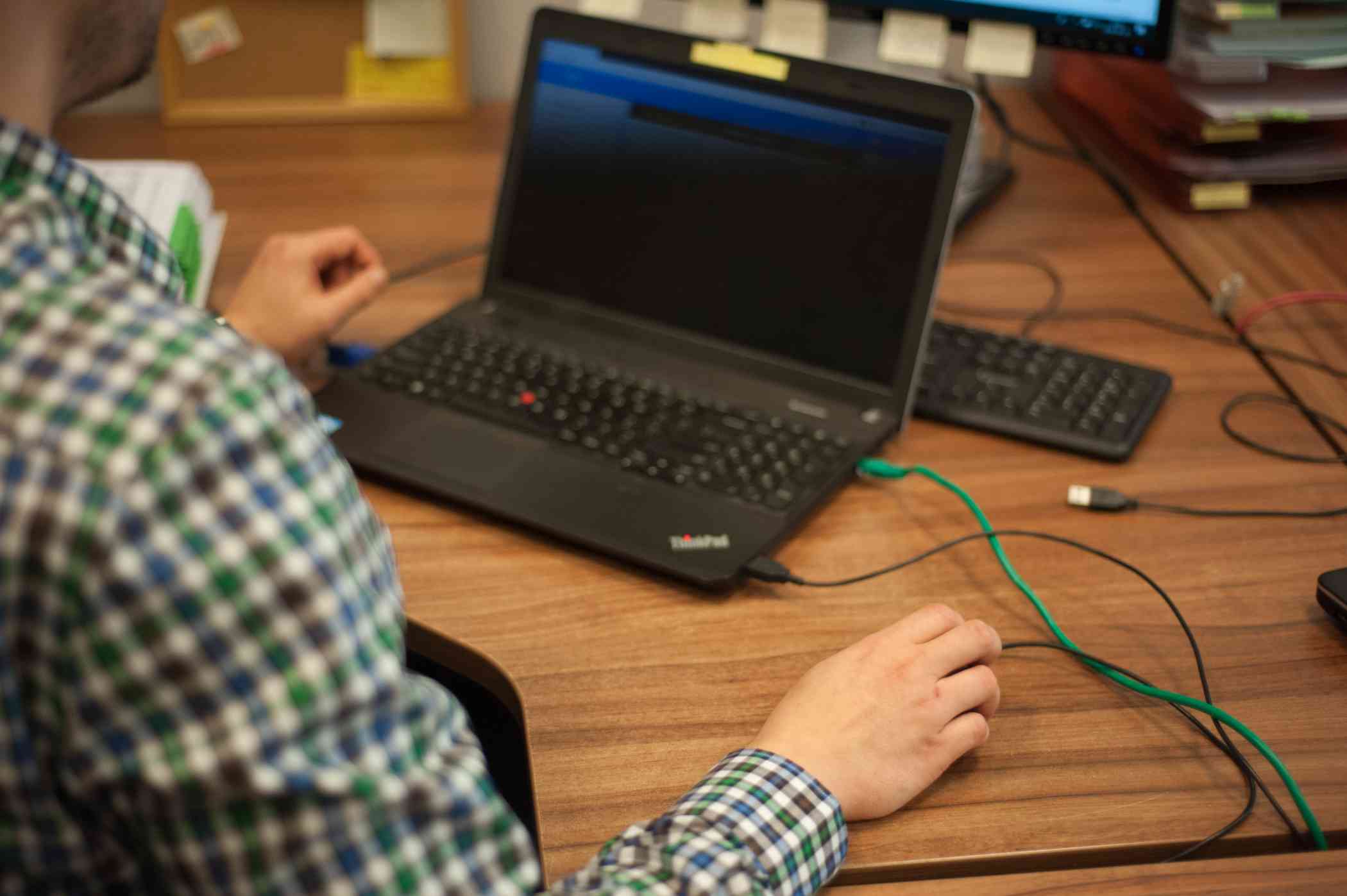 Laptop stojący na biurku, widok ręki, kt&oacute;ra trzyma mysz komputerową i robi coś na komputerze