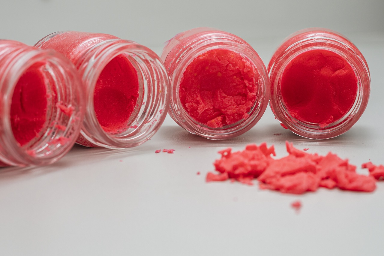 Otwarte małe słoiczki z czerwonym proszkiem, kt&oacute;re leżą na stole