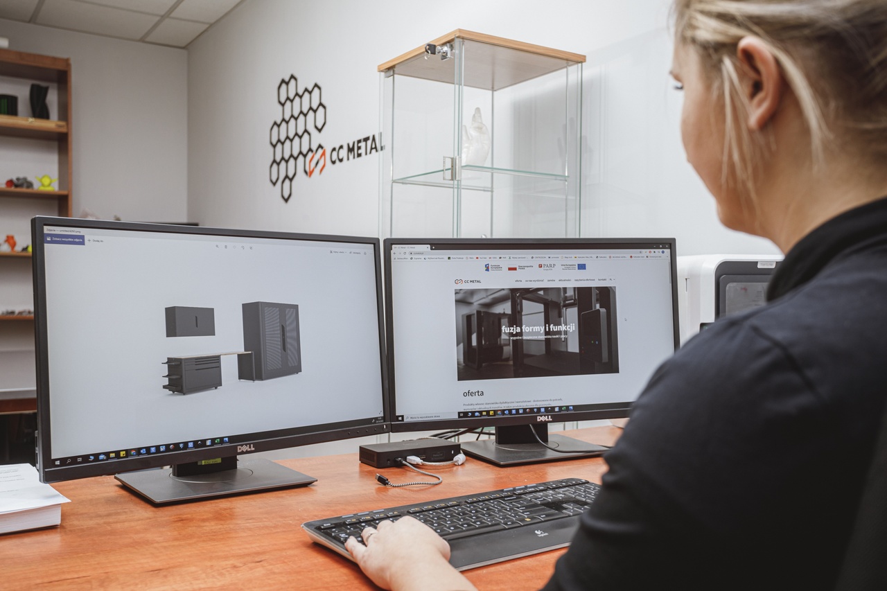 Kobieta siedzi przed dwoma ekranami od komputer&oacute;w