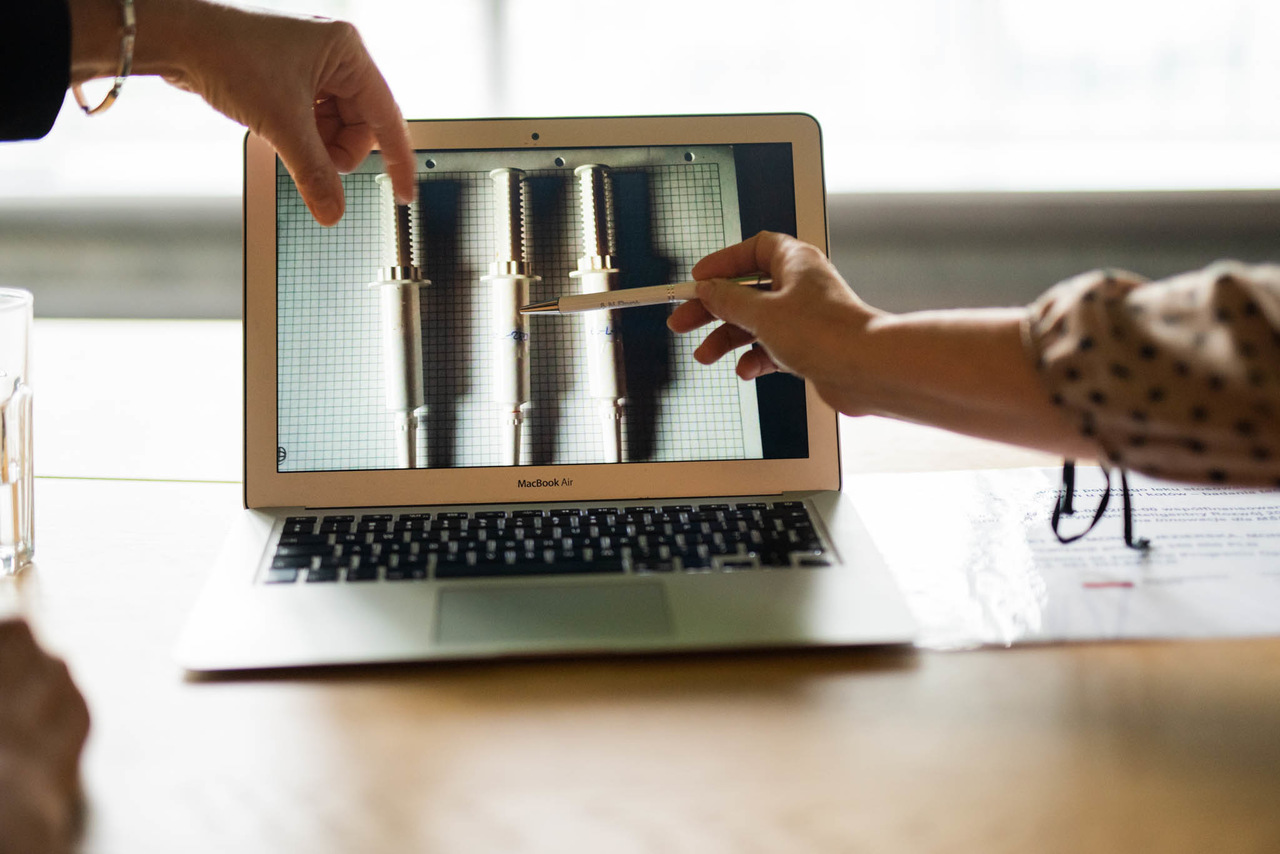 Laptop stoi na biurku, wok&oacute;ł ręce, kt&oacute;re wskazują na ekran.