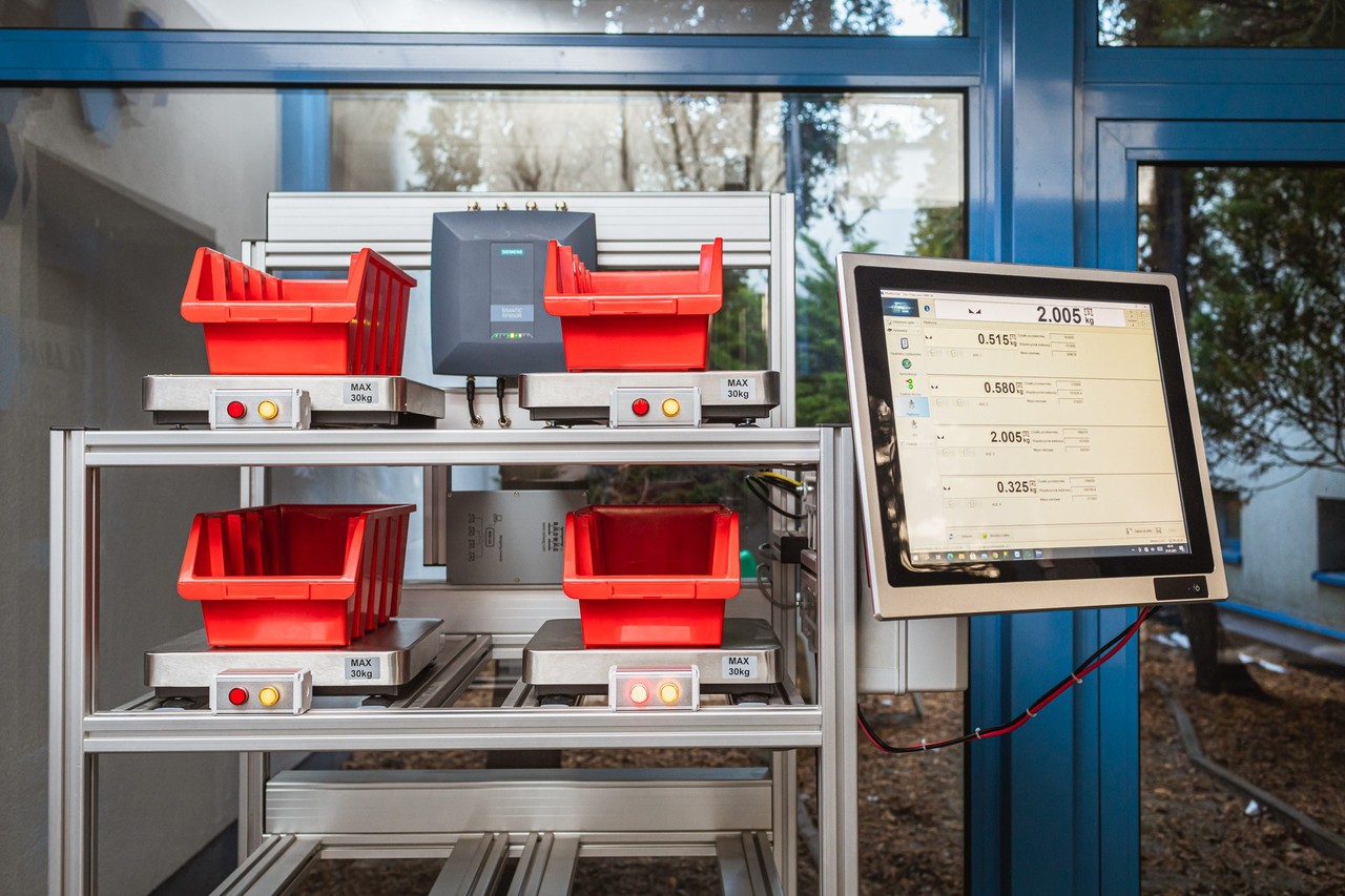 Pojemniki stojące na p&oacute;lkach, przy nich monitor